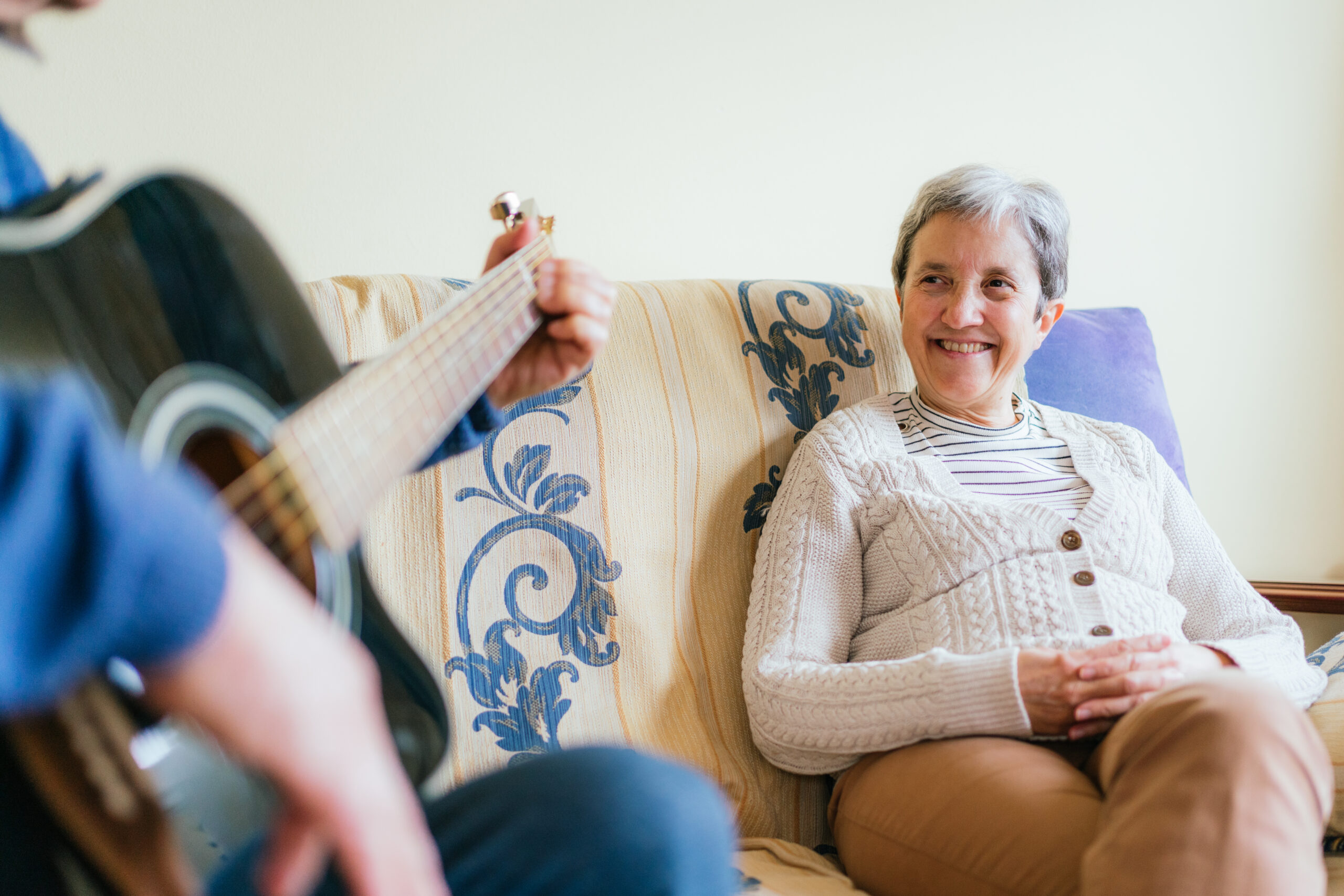 Adult male playing the guitar for his wife sitting on a couch in the house adult male playing the guitar for his wife sitting 2025 02 11 19 34 21 utc scaled